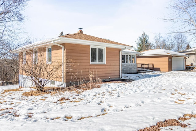 snow covered rear of property featuring a detached garage, an outdoor structure, and roof with shingles