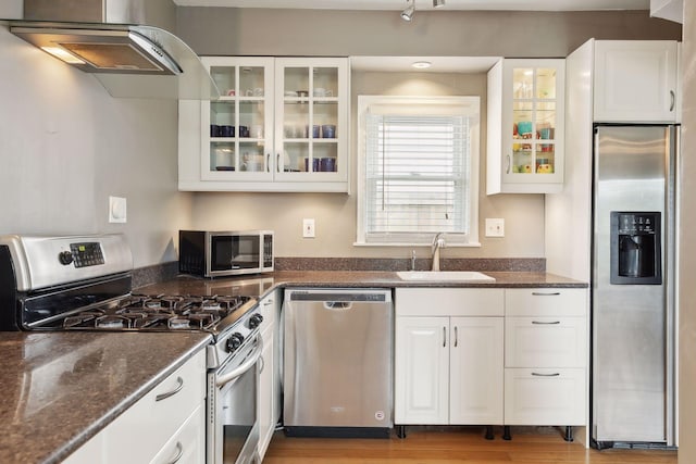 kitchen featuring appliances with stainless steel finishes, dark stone counters, ventilation hood, sink, and white cabinetry