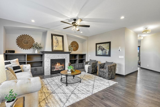 living room with a stone fireplace, ceiling fan, and dark wood-type flooring