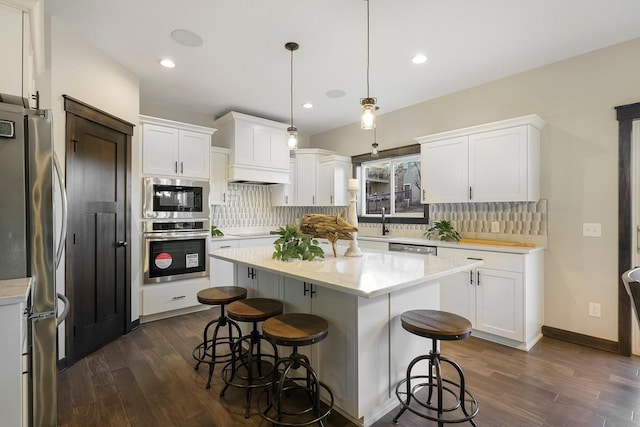 kitchen featuring a center island, dark wood-type flooring, hanging light fixtures, white cabinetry, and stainless steel appliances