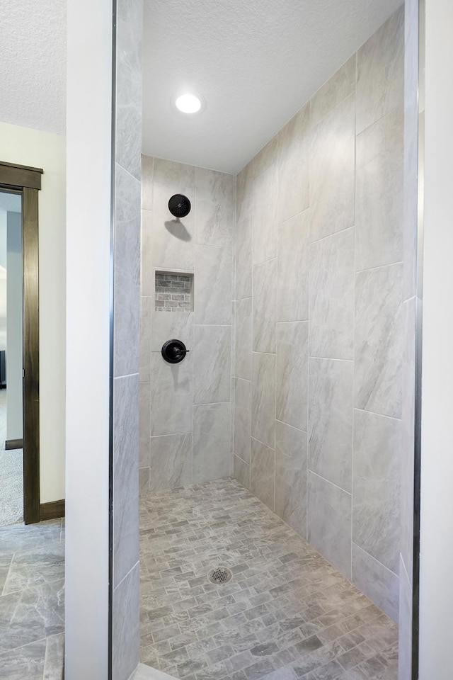 bathroom with a textured ceiling and tiled shower