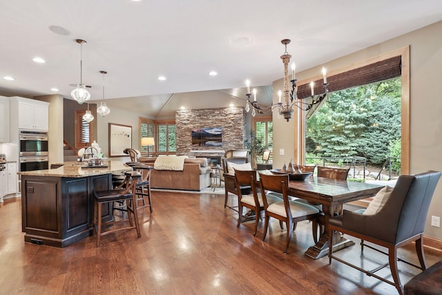 dining room featuring an inviting chandelier, dark hardwood / wood-style floors, and a stone fireplace