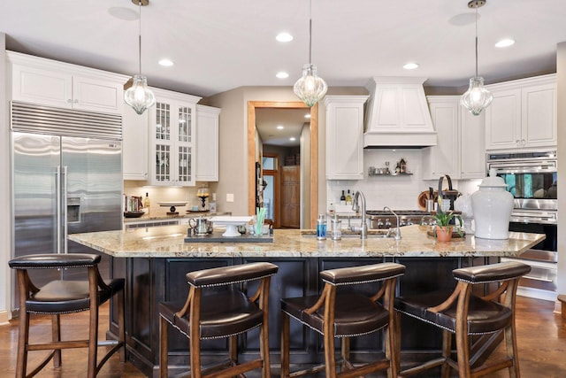 kitchen with premium range hood, hanging light fixtures, stainless steel appliances, a spacious island, and white cabinets