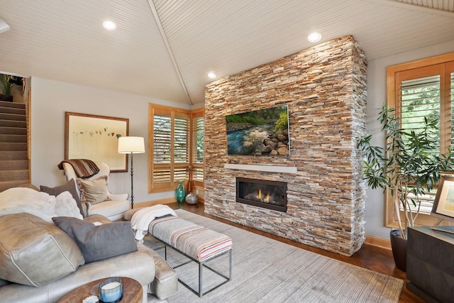 living room featuring hardwood / wood-style flooring, vaulted ceiling, and a stone fireplace