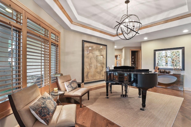 living area with an inviting chandelier, ornamental molding, a raised ceiling, and hardwood / wood-style floors