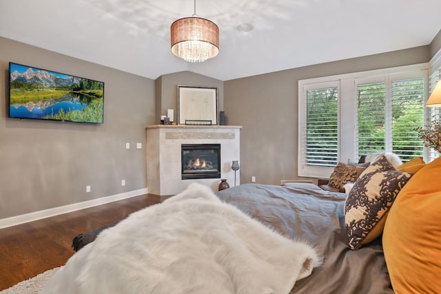 bedroom with dark wood-type flooring, lofted ceiling, a tile fireplace, and a notable chandelier