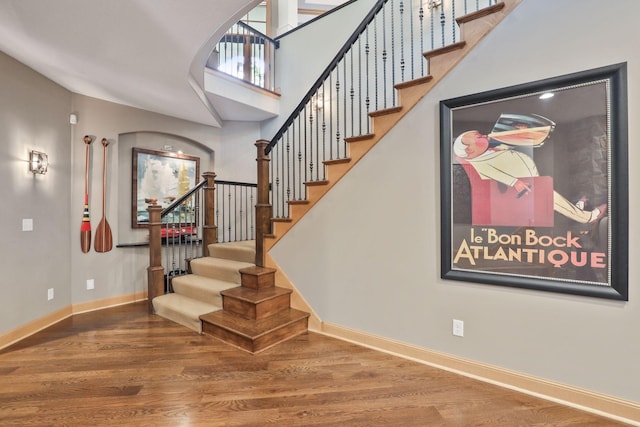 staircase with wood-type flooring and a towering ceiling