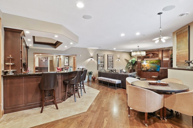 dining space with indoor bar, light hardwood / wood-style floors, and a tray ceiling