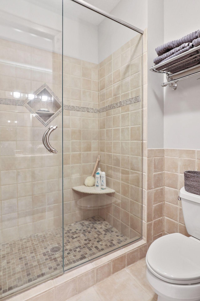 bathroom with tile patterned floors, toilet, a shower with door, and tile walls