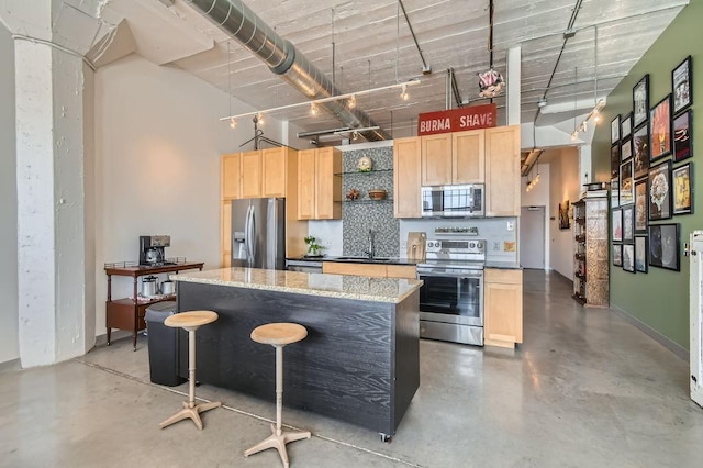 kitchen with appliances with stainless steel finishes, a center island, light stone countertops, finished concrete floors, and light brown cabinetry