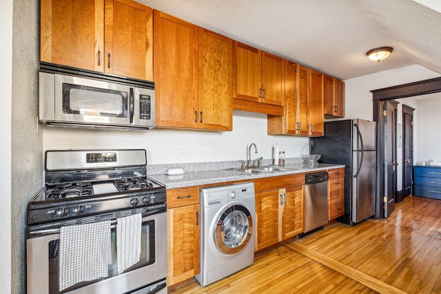 kitchen with sink, stainless steel appliances, washer / clothes dryer, light hardwood / wood-style floors, and a textured ceiling