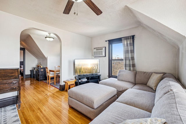 living room with a textured ceiling, a wall unit AC, ceiling fan, vaulted ceiling, and hardwood / wood-style flooring