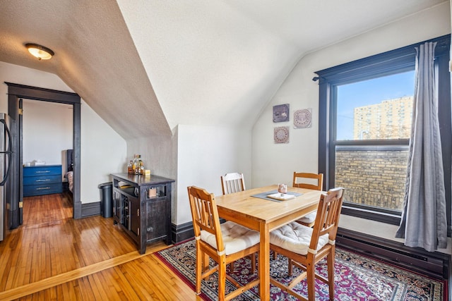 dining room featuring hardwood / wood-style flooring, lofted ceiling, a textured ceiling, and a wealth of natural light