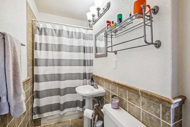 bathroom featuring a textured ceiling, toilet, tile walls, and walk in shower