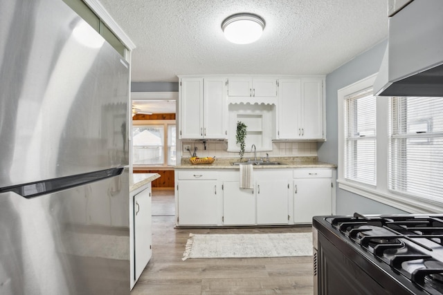 kitchen with light wood finished floors, white cabinets, a wealth of natural light, and freestanding refrigerator