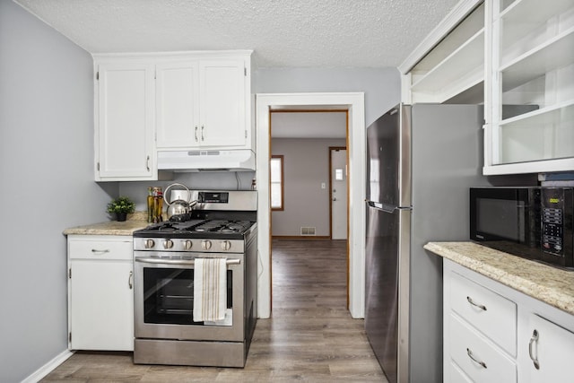 kitchen featuring white cabinets, wood finished floors, black microwave, under cabinet range hood, and gas range