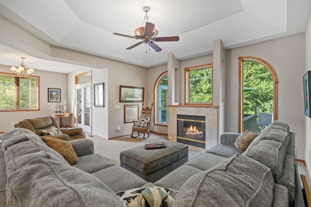 living room featuring light colored carpet, a raised ceiling, ceiling fan with notable chandelier, and a tile fireplace