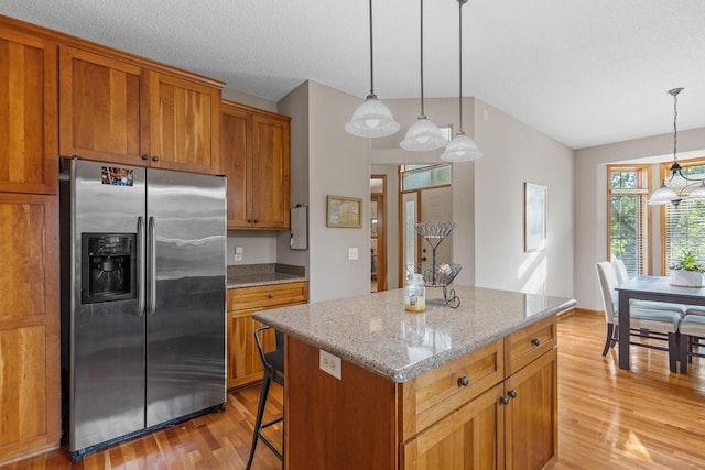 kitchen with a kitchen island, decorative light fixtures, light stone counters, and stainless steel fridge with ice dispenser