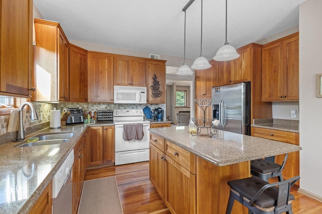 kitchen featuring sink, decorative light fixtures, a center island, stainless steel appliances, and light hardwood / wood-style floors