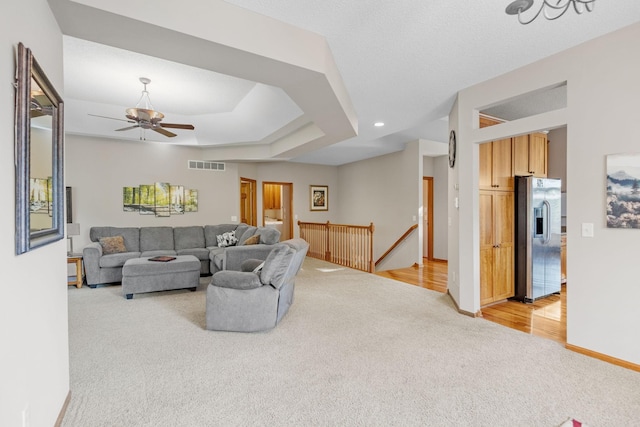 living area featuring baseboards, visible vents, a raised ceiling, light colored carpet, and ceiling fan