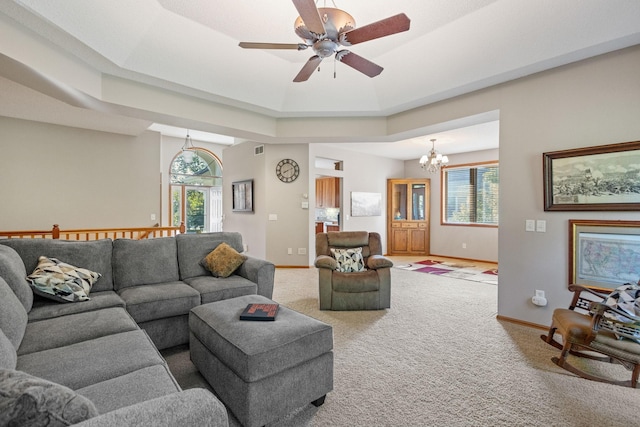 carpeted living area featuring ceiling fan with notable chandelier, a tray ceiling, visible vents, and baseboards