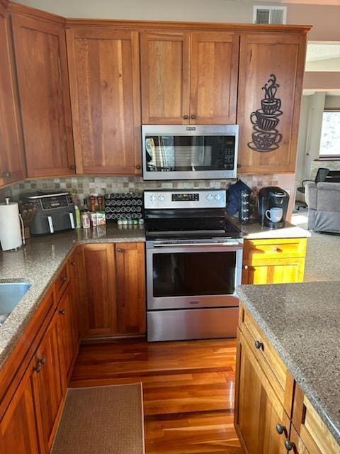 kitchen with light stone counters, visible vents, light wood-style floors, appliances with stainless steel finishes, and tasteful backsplash