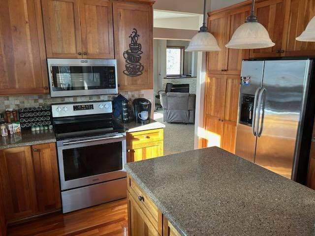 kitchen with brown cabinets, decorative light fixtures, stainless steel appliances, tasteful backsplash, and wood finished floors