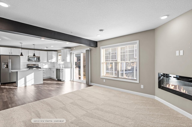 unfurnished living room with beam ceiling, a textured ceiling, hardwood / wood-style flooring, and sink