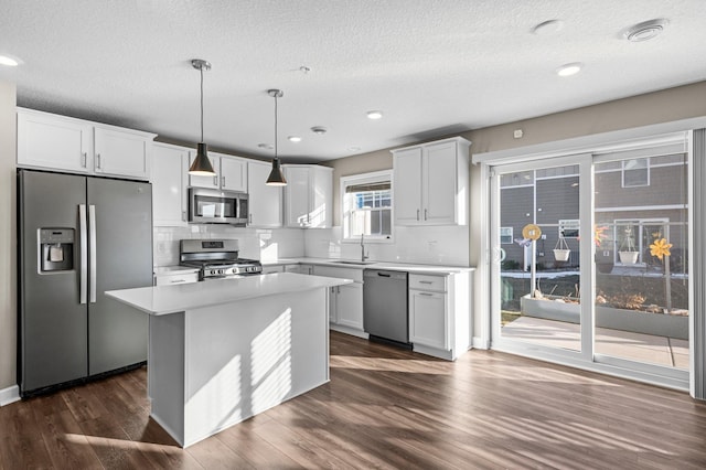 kitchen featuring appliances with stainless steel finishes, backsplash, a kitchen island, decorative light fixtures, and white cabinetry