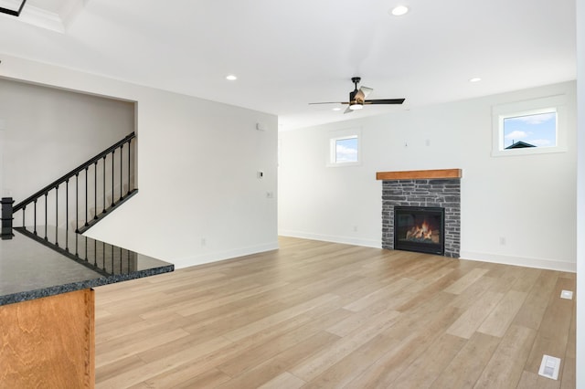 unfurnished living room featuring light hardwood / wood-style floors, a stone fireplace, and ceiling fan