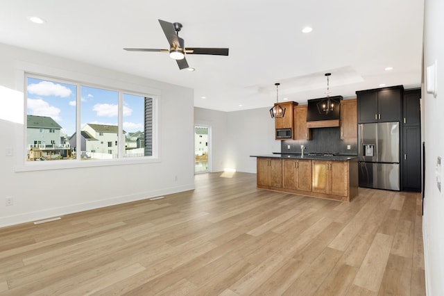 kitchen featuring backsplash, stainless steel appliances, a kitchen island with sink, decorative light fixtures, and light hardwood / wood-style flooring