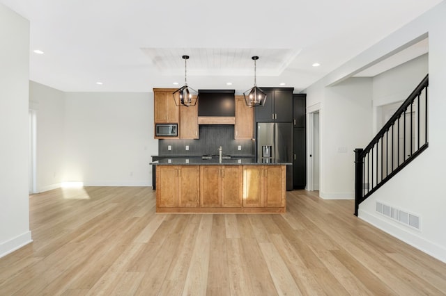 kitchen featuring appliances with stainless steel finishes, light wood-type flooring, a center island with sink, an inviting chandelier, and hanging light fixtures