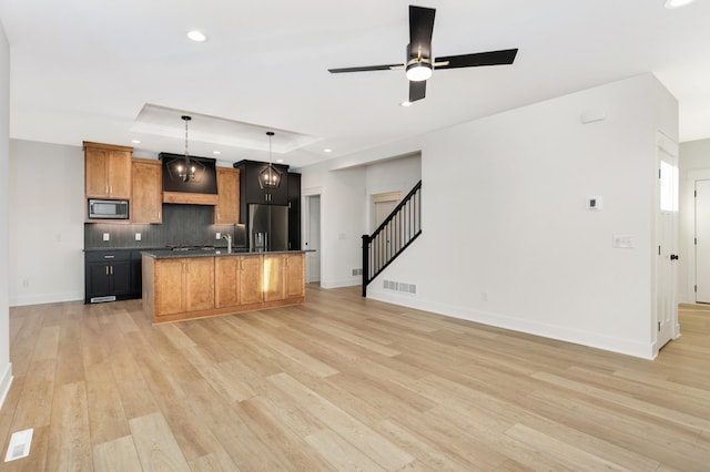 kitchen featuring ceiling fan, stainless steel appliances, a raised ceiling, decorative light fixtures, and a kitchen island with sink