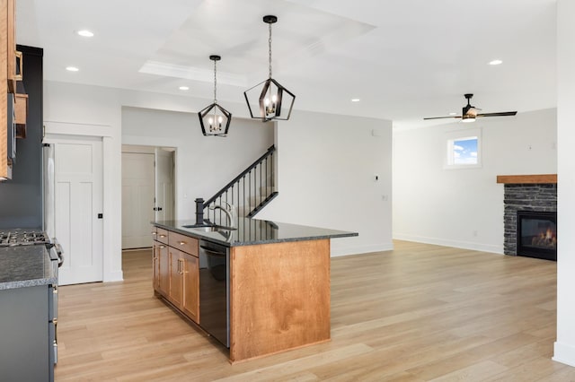 kitchen featuring ceiling fan, dishwasher, a fireplace, hanging light fixtures, and an island with sink