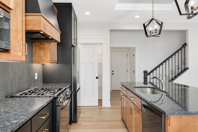 kitchen featuring sink, premium range hood, dark stone counters, decorative light fixtures, and appliances with stainless steel finishes