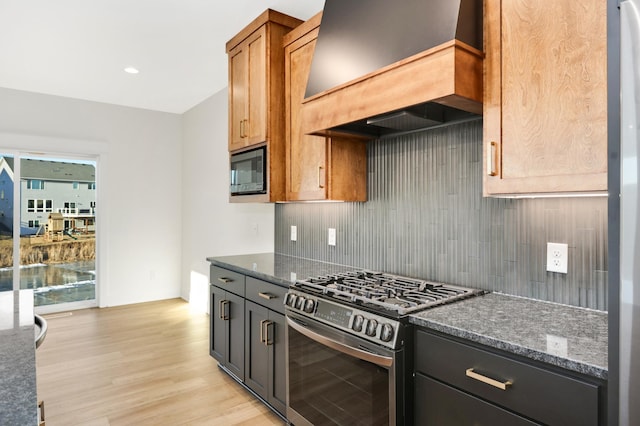 kitchen featuring backsplash, premium range hood, built in microwave, dark stone countertops, and stainless steel range with gas stovetop