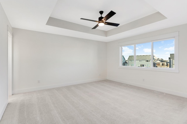 empty room featuring ceiling fan, a raised ceiling, and light colored carpet