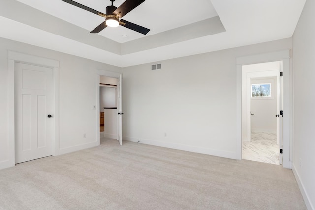 unfurnished bedroom featuring ceiling fan, a raised ceiling, and light colored carpet