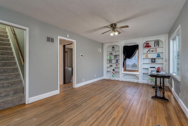 interior space with built in shelves, a textured ceiling, ceiling fan, hardwood / wood-style flooring, and plenty of natural light