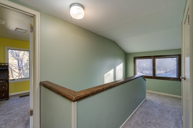 hallway featuring a textured ceiling, light colored carpet, and vaulted ceiling