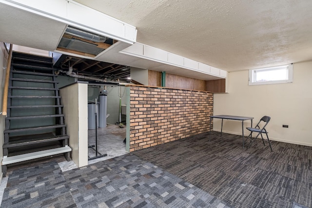 basement featuring dark colored carpet, a textured ceiling, and brick wall