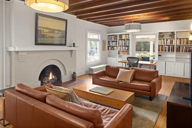 living area featuring a wealth of natural light, a brick fireplace, wood finished floors, and beamed ceiling