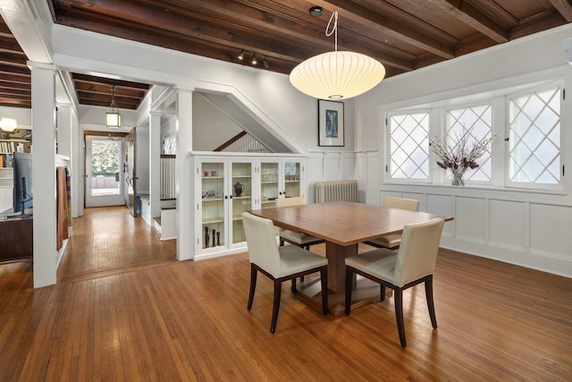 dining space featuring radiator heating unit, a decorative wall, hardwood / wood-style floors, and beamed ceiling