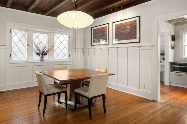 dining space featuring beamed ceiling, wood-type flooring, and a decorative wall