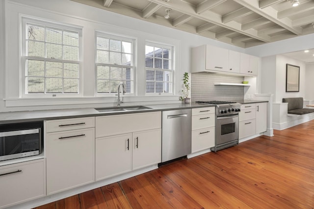 kitchen featuring hardwood / wood-style flooring, stainless steel appliances, a sink, decorative backsplash, and dark countertops