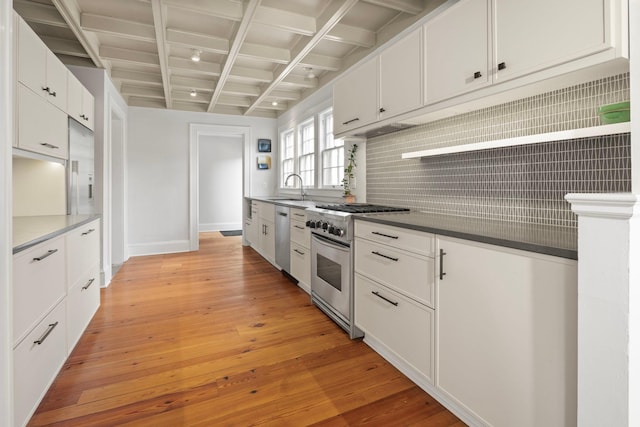 kitchen with light wood finished floors, backsplash, appliances with stainless steel finishes, white cabinets, and beamed ceiling