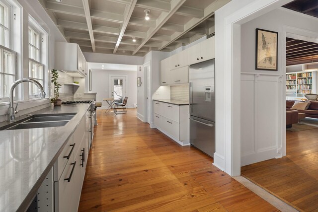 kitchen with premium appliances, light wood-style floors, a sink, and tasteful backsplash