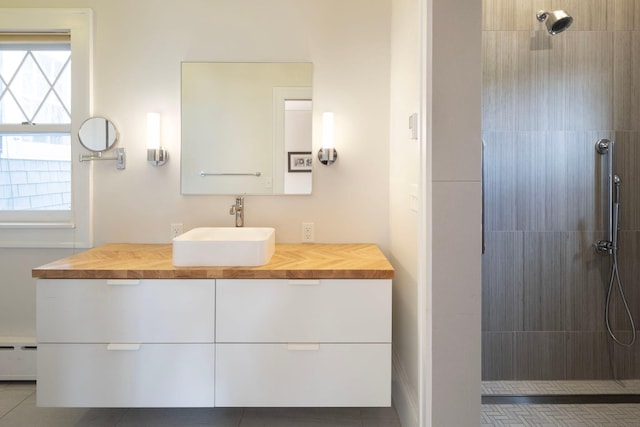 full bath with a baseboard heating unit, tiled shower, and vanity