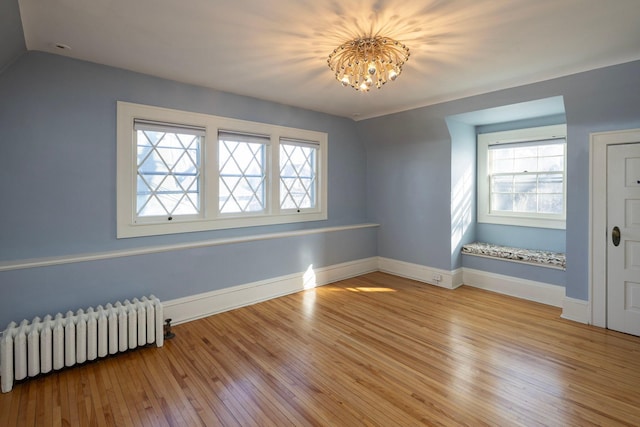 spare room featuring baseboards, radiator, lofted ceiling, wood-type flooring, and a chandelier