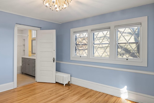 unfurnished bedroom with an inviting chandelier, radiator heating unit, multiple windows, and light wood-style flooring